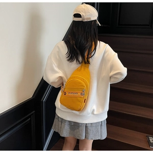 Mannequin portant un sac bandoulière jaune en toile avec sangle à lettres sur un escalier