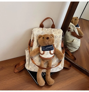 Detail of cream backpack with bear prints featuring a plush bear charm on wood table