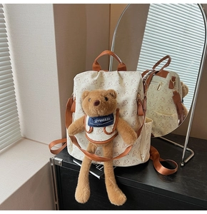 Detail view of cream backpack featuring cartoon bear print and 3D plush bear ornament