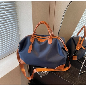 Close-up of a blue canvas travel bag with brown leather handles and adjustable shoulder strap