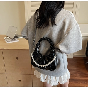 Detail of a black shiny ruched bag featuring a large decorative pearl chain on a desk