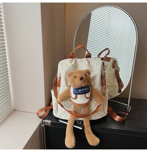 Detail of canvas backpack with bear print, brown leather handles and plush bear charm