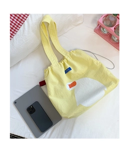 Flat lay of yellow canvas tote bag with duck print and drawstring on white bedding