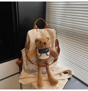 Detail view of cream backpack featuring all-over bear print and large plush bear ornament