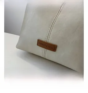 Detail showing textured cream leather, vertical stitching, and a brown embossed brand logo tag