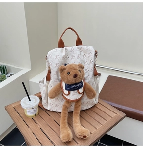 Close-up of printed backpack featuring a cute brown plush bear charm and leather zipper detail