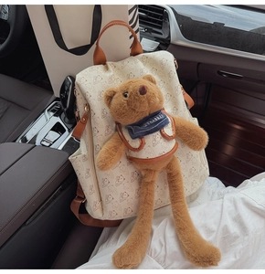 Detail shot of a cream backpack with bear print and long-legged plush bear charm on a car seat
