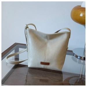 Detail of cream bucket bag showing leather grain texture and branded logo patch on the front