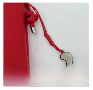 Détail d'un sac en cuir rouge grainé avec nœud tressé et pendentif haricot en métal argenté