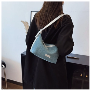 Dettaglio della borsa hobo in denim blu con tracolla in pelle bianca e logo in metallo