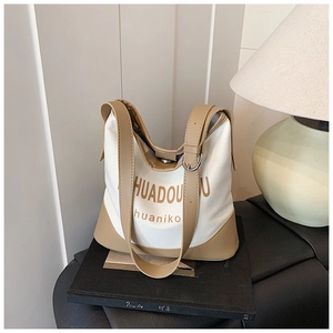 Detail of white canvas tote with camel leather trim and adjustable shoulder strap on books