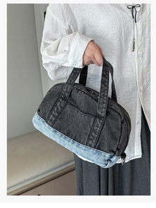 Detail of a color-block denim handbag featuring a dual-tone design and functional outer pocket
