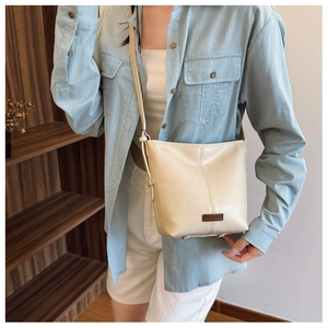 Detail of creamy PU leather bucket bag featuring pebbled texture and branded logo patch