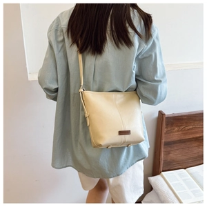 Detail of cream leather bucket bag showing refined texture and brand logo tag