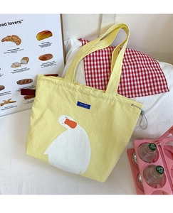 Close-up of yellow canvas tote bag featuring a cute white duck and blue logo tag