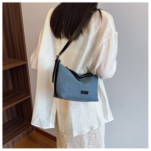 Dettaglio della borsa hobo in denim blu con tracolla in pelle nera e tessuto strutturato