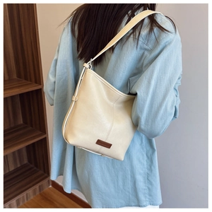 Close-up of beige hobo shoulder bag featuring a dark brown leather logo patch detail