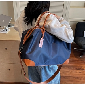 Detail of blue nylon travel bag featuring leather trim and adjustable shoulder strap on model