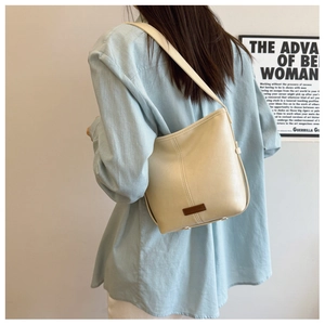 Detail view of a cream leather bucket bag with brown logo patch worn by a model