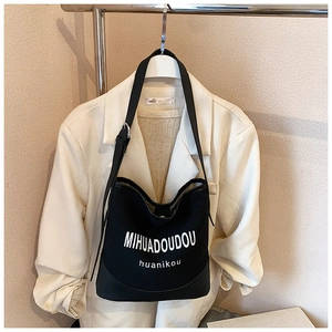 Detailed view of black canvas crossbody bag featuring white printed text and wide strap
