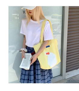 Detail of yellow canvas tote bag with white duck pattern worn with casual outfit