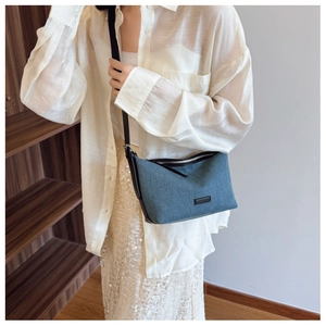 Dettaglio borsa a tracolla in denim blu con cinturino in pelle nera e chiusura a cerniera