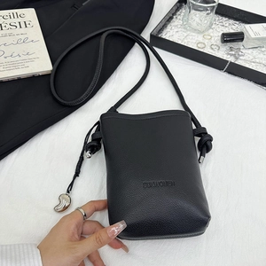 Détail du mini sac bandoulière en cuir noir avec logo embossé et pendentif métallique
