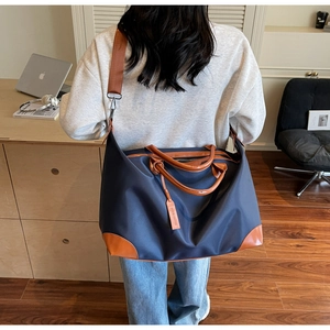 Deep blue nylon travel bag with brown leather handles and adjustable shoulder strap worn by model