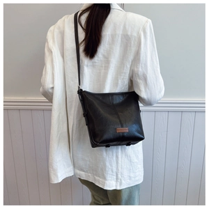 Detail view of the black bucket bag with a brown leather tag on a stylish model
