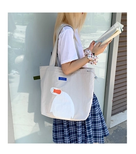 Detail view of large white duck cartoon print on a light gray canvas tote bag with side drawstrings