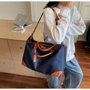 Detail of navy nylon travel bag featuring brown leather handles and adjustable shoulder strap