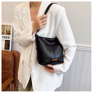 Detail of minimalist black faux leather shoulder bag with vertical stitching and logo tag
