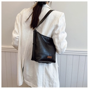 Detailed view of black faux leather bucket bag with brown brand tag on a white blazer