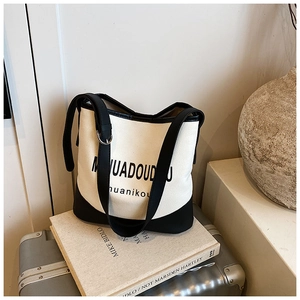 Detail of canvas bucket bag with black leather trim resting on luggage for travel