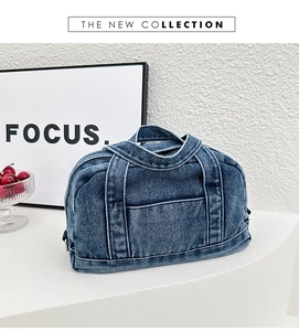 Detail view of a vintage blue denim handbag with front pocket on a white pedestal