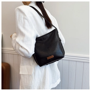 Classic black leather bucket bag with brand logo tag worn on a white suit jacket