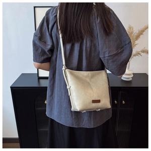 Rear view of cream leather crossbody bucket bag worn with adjustable shoulder strap