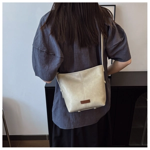 Detail view of cream bucket bag in pebbled faux leather with brand logo patch