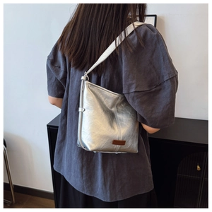 Detail of silver metallic shoulder bag showing crinkled texture and brown logo patch