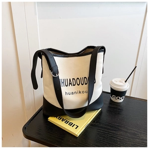 Detailed view of canvas and black leather crossbody tote bag on a dark wooden table