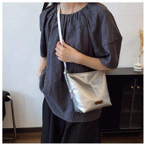 Detailed view of silver metallic bucket bag with micro-pleated texture and brown logo patch