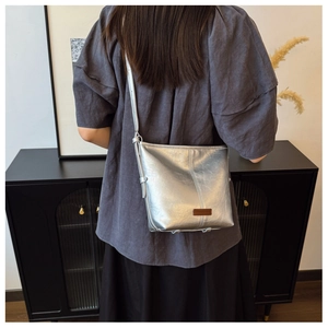Close-up of metallic silver bucket bag with brown logo patch and adjustable strap