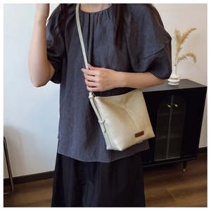 Detail of beige textured leather bucket bag with adjustable strap on a model