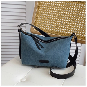 Dettaglio della borsa in denim blu con manici in pelle nera e chiusura a zip argentata