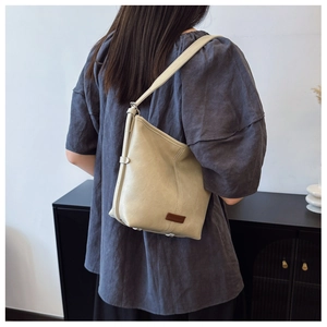 Detail of cream leather bucket bag showing premium pebbled texture and logo patch