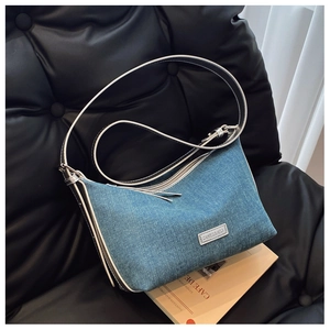 Dettaglio borsa a mezzaluna in denim azzurro con cuciture bianche a contrasto su divano nero
