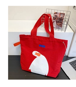 Detailed view of a red canvas tote bag with a cute white duck print and orange handles