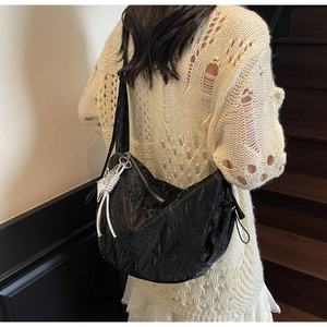 Detail of crinkled black crescent shoulder bag featuring a silver butterfly charm pendant