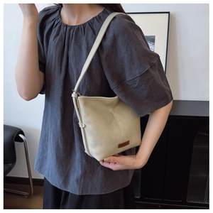Detail shot of a cream white leather bucket bag worn on shoulder with minimal logo