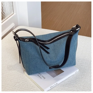 Dettaglio borsa a mezzaluna in denim blu con tracolla in pelle nera e cerniera argentata